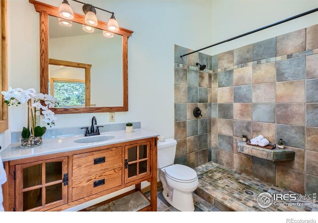 bathroom featuring a tile shower, vanity, and toilet