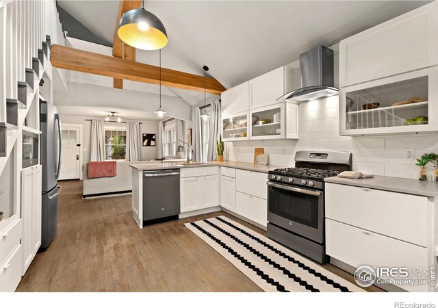 kitchen featuring vaulted ceiling, appliances with stainless steel finishes, wall chimney range hood, and kitchen peninsula