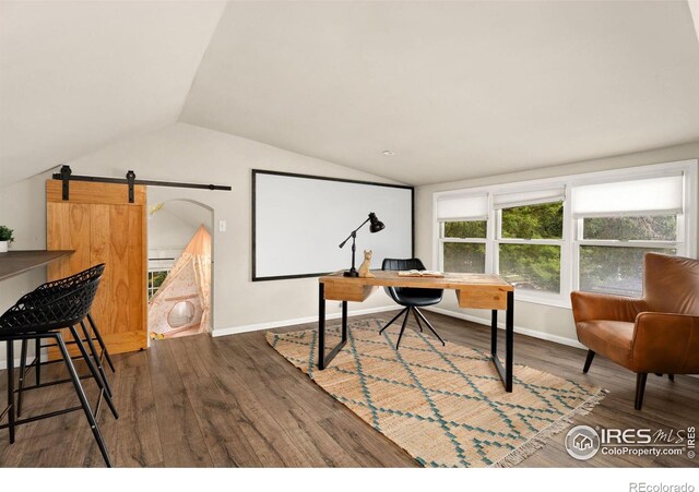 office area featuring wood-type flooring, vaulted ceiling, and a barn door