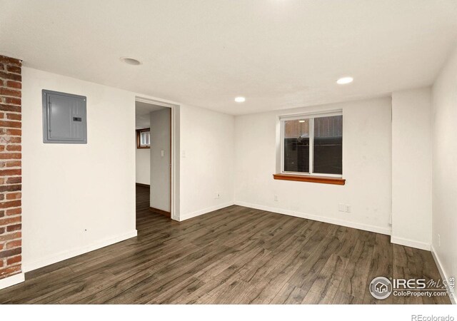 empty room featuring brick wall, electric panel, and dark wood-type flooring