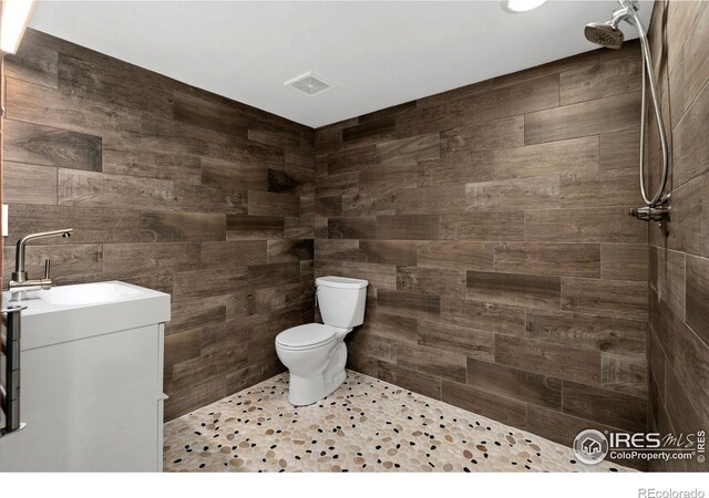 bathroom with vanity, tile walls, toilet, and tiled shower