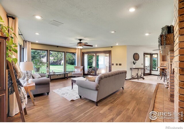 living room with light hardwood / wood-style flooring, a wealth of natural light, ceiling fan, and a textured ceiling