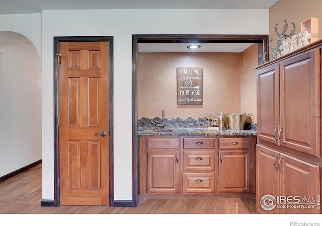 kitchen featuring light wood-type flooring, dark stone counters, brown cabinets, and baseboards