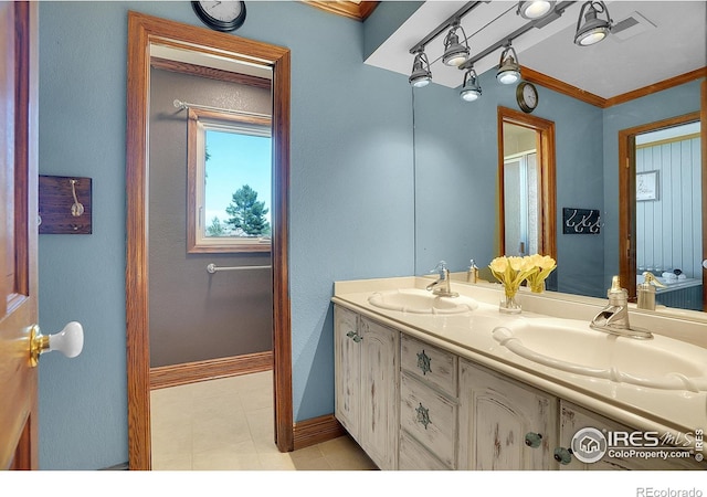 bathroom featuring double vanity, crown molding, baseboards, and a sink