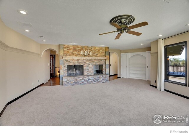 unfurnished living room with light carpet, a textured ceiling, ceiling fan, and a stone fireplace