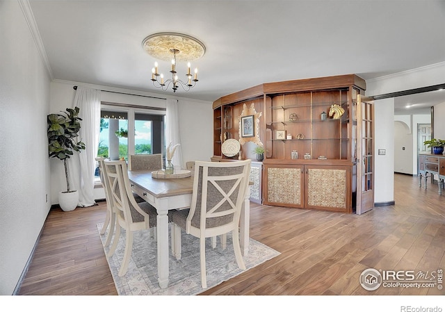 dining area with arched walkways, a chandelier, wood finished floors, and ornamental molding