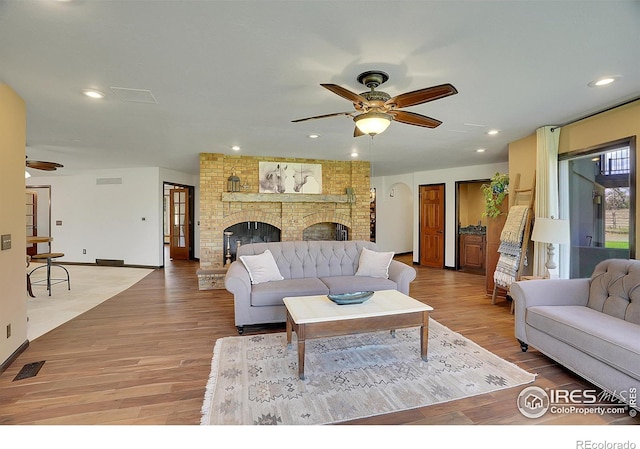 living room with a ceiling fan, light wood-type flooring, a brick fireplace, and visible vents