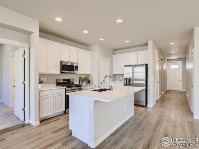 kitchen with a kitchen island with sink, a sink, white cabinetry, light countertops, and appliances with stainless steel finishes