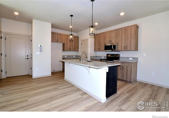 kitchen with pendant lighting, appliances with stainless steel finishes, a center island with sink, sink, and light hardwood / wood-style floors