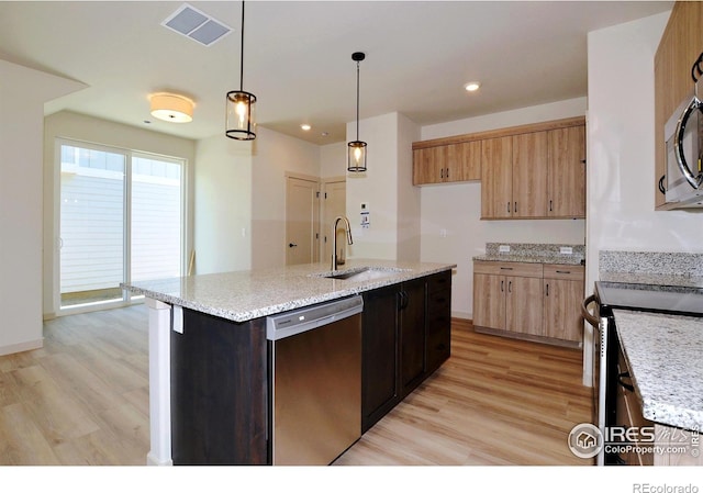 kitchen with light wood-type flooring, appliances with stainless steel finishes, an island with sink, sink, and decorative light fixtures