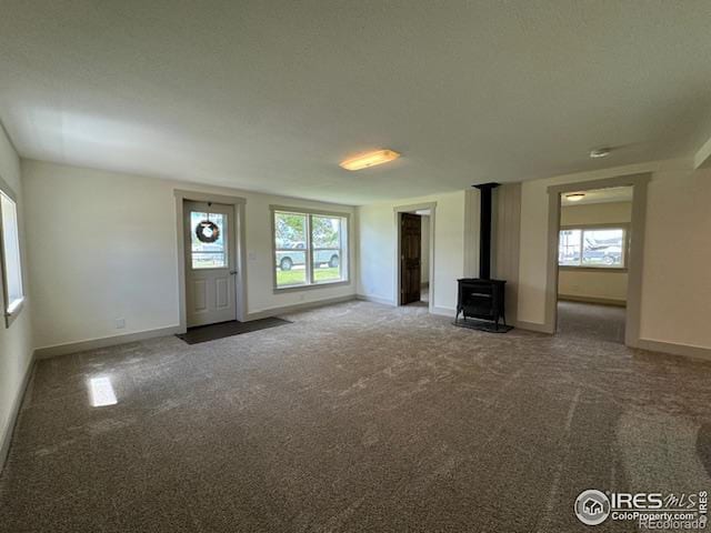 unfurnished living room with carpet floors, a healthy amount of sunlight, and a wood stove