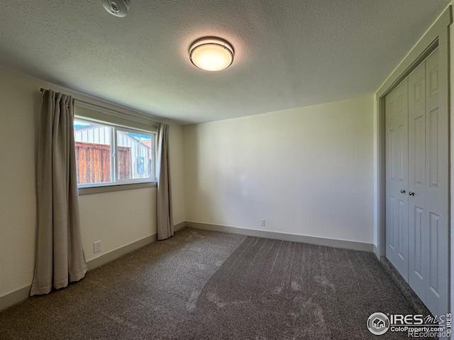 unfurnished bedroom with a textured ceiling, dark carpet, and a closet