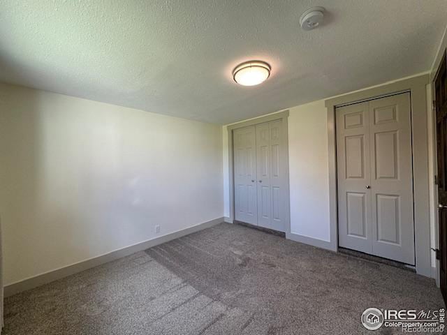 unfurnished bedroom featuring a textured ceiling, carpet flooring, and two closets