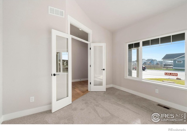 unfurnished bedroom featuring vaulted ceiling, light carpet, and french doors