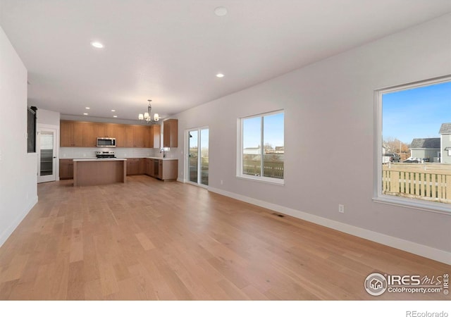 unfurnished living room with an inviting chandelier, sink, and light hardwood / wood-style flooring