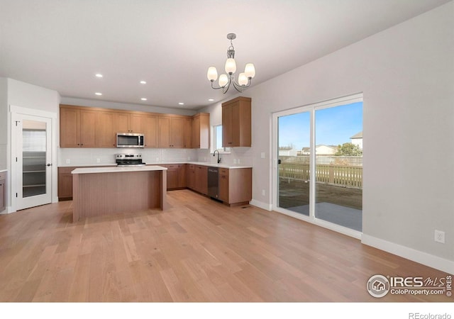 kitchen featuring decorative light fixtures, stainless steel appliances, a kitchen island, and light hardwood / wood-style floors