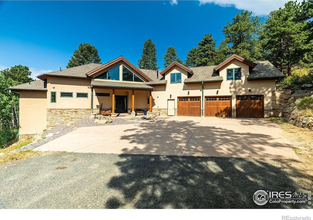 view of front facade featuring driveway, stone siding, a garage, and stucco siding