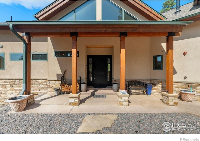 view of exterior entry with stone siding, a patio, and stucco siding