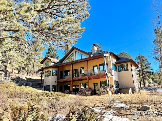 back of property with a garage, a chimney, a balcony, and stucco siding