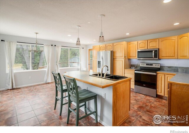 kitchen featuring a kitchen island with sink, a sink, hanging light fixtures, appliances with stainless steel finishes, and light countertops