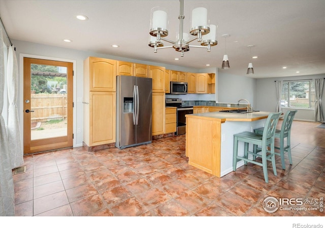 kitchen featuring light countertops, appliances with stainless steel finishes, light brown cabinetry, an island with sink, and pendant lighting