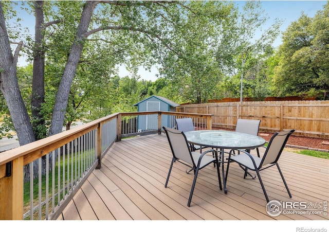 deck with an outbuilding, outdoor dining space, fence, and a storage shed