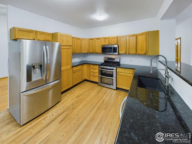 kitchen featuring dark stone countertops, sink, light wood-type flooring, and appliances with stainless steel finishes