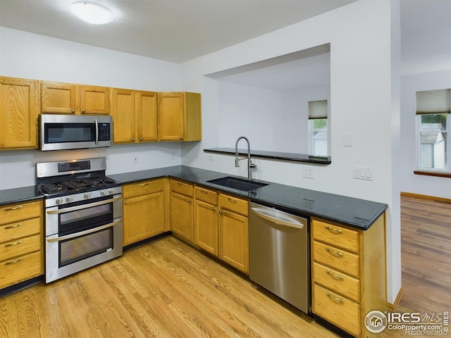 kitchen featuring light wood-type flooring, sink, appliances with stainless steel finishes, and dark stone counters