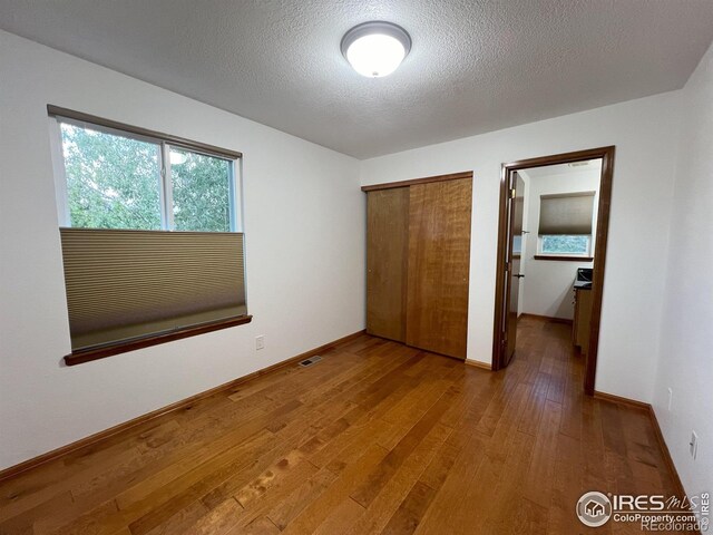 unfurnished bedroom with wood-type flooring, a textured ceiling, and a closet