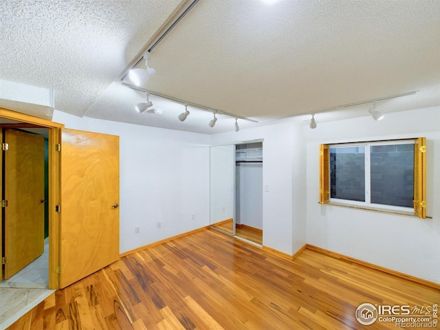 unfurnished bedroom featuring rail lighting, light wood-type flooring, a textured ceiling, and a closet