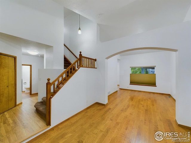 interior space with arched walkways, a towering ceiling, baseboards, and wood finished floors