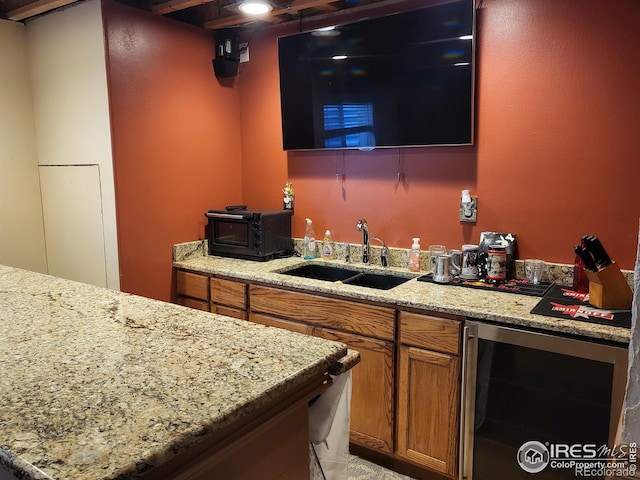 kitchen featuring light stone countertops, wine cooler, brown cabinetry, and a sink