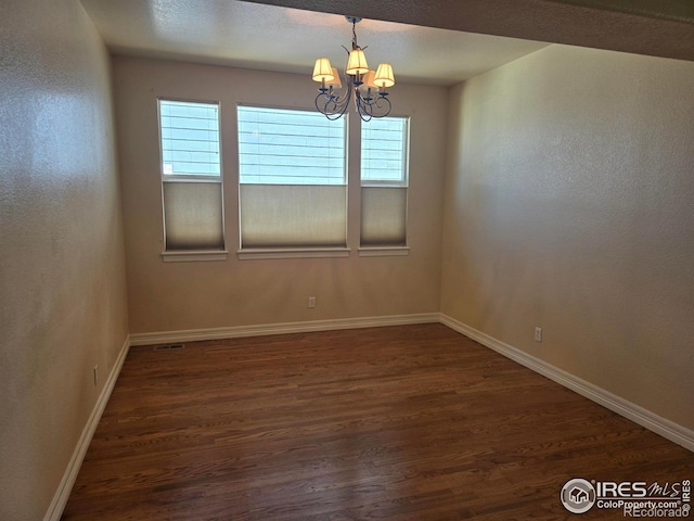 empty room featuring a wealth of natural light, a chandelier, and dark wood-type flooring