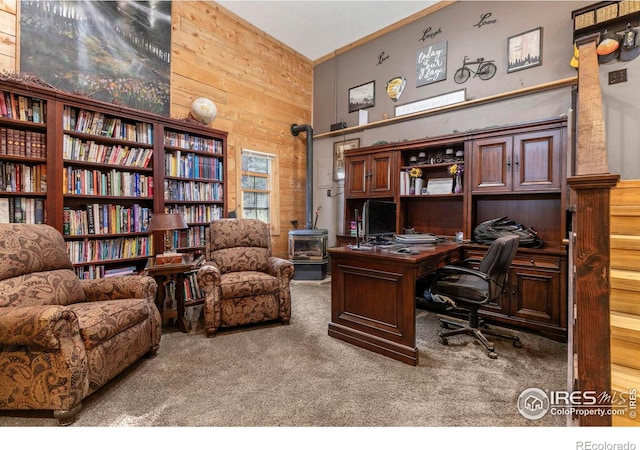 carpeted office space featuring a wood stove and wooden walls