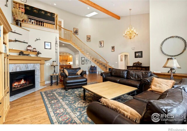 living room with high vaulted ceiling, an inviting chandelier, a fireplace, beamed ceiling, and light hardwood / wood-style flooring