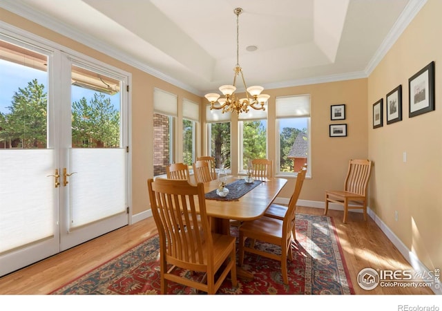 dining room featuring light wood-type flooring, a chandelier, ornamental molding, and a tray ceiling