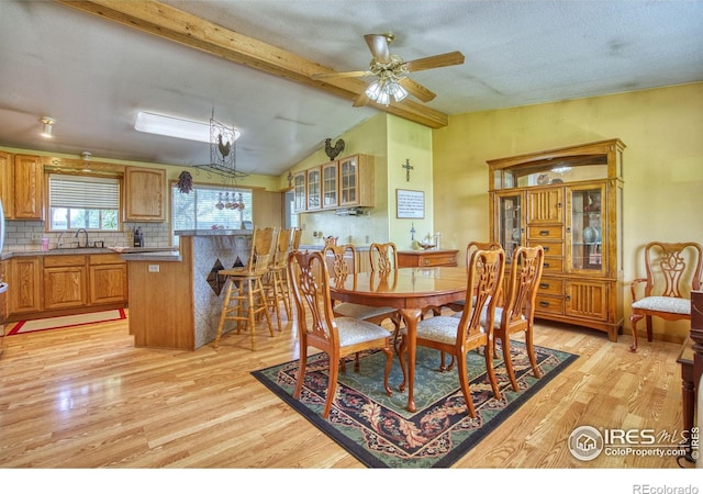 dining space with ceiling fan, light hardwood / wood-style flooring, sink, and lofted ceiling with beams