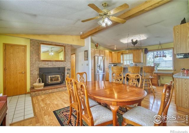 dining room with ceiling fan, vaulted ceiling with beams, light wood-type flooring, and a brick fireplace