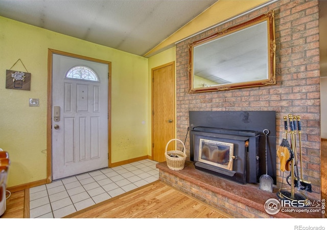 tiled foyer entrance with vaulted ceiling and a wood stove