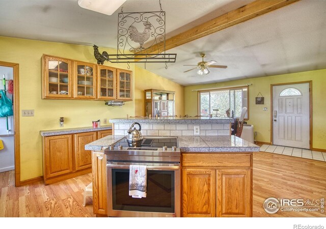 kitchen featuring light wood-type flooring, vaulted ceiling with beams, ceiling fan, and stainless steel range with electric cooktop