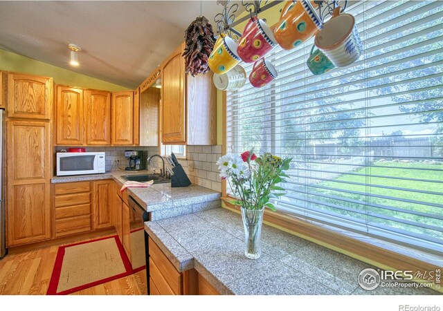 kitchen with sink, light hardwood / wood-style flooring, vaulted ceiling, tasteful backsplash, and dishwasher