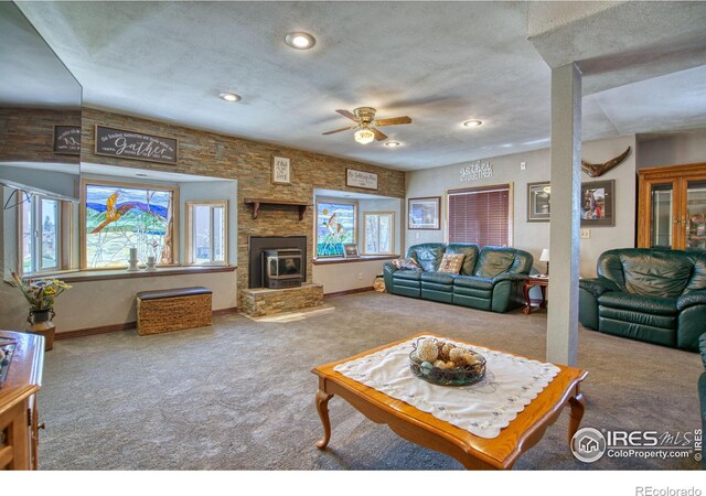 carpeted living room featuring ceiling fan, a textured ceiling, and a stone fireplace