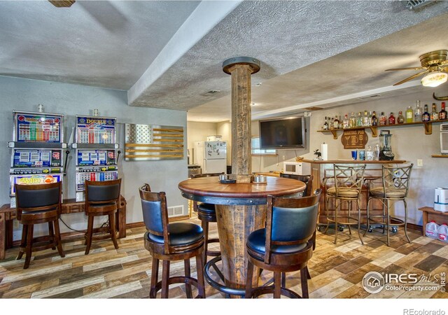 dining space with ceiling fan, light wood-type flooring, a textured ceiling, and bar area