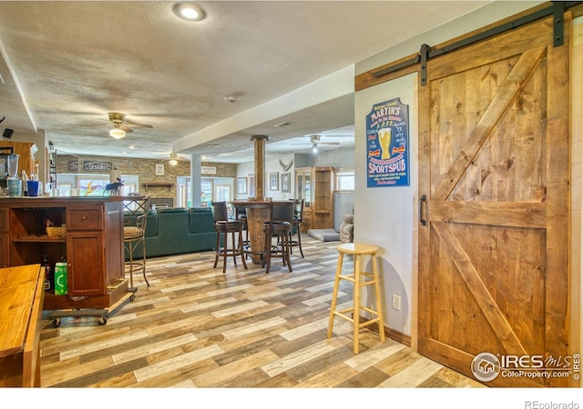 interior space with a textured ceiling, ceiling fan, light wood-type flooring, and a barn door