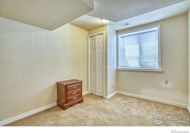 interior space with light colored carpet, a closet, and a textured ceiling