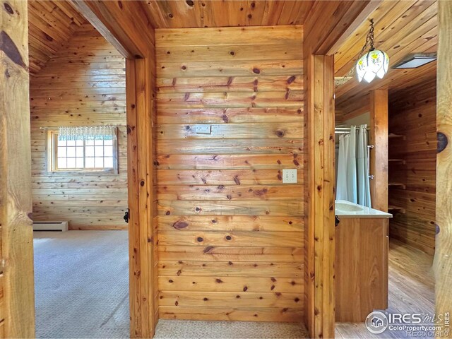 hallway featuring light carpet, baseboard heating, wooden walls, and wood ceiling