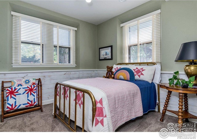 bedroom featuring multiple windows, carpet flooring, and wood walls