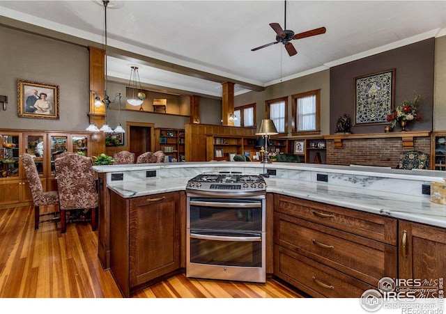 kitchen with light hardwood / wood-style flooring, ceiling fan, double oven range, light stone counters, and decorative light fixtures