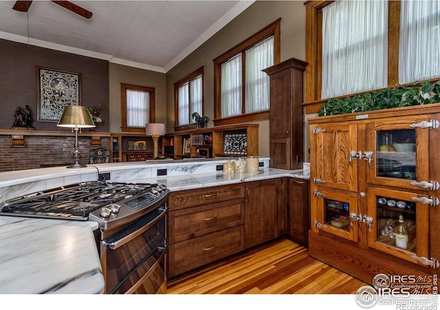 kitchen with range with two ovens, ornamental molding, ceiling fan, light stone counters, and light wood-type flooring