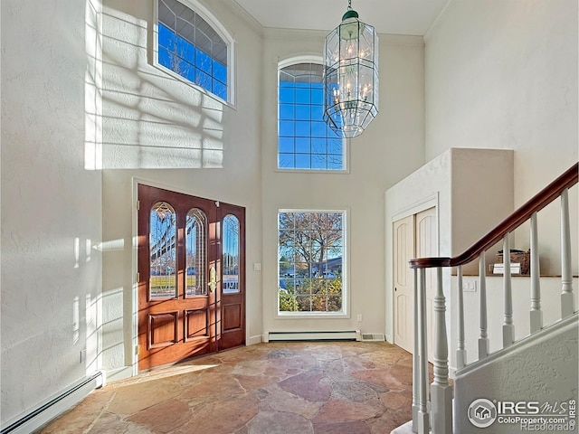 foyer featuring crown molding, a baseboard heating unit, an inviting chandelier, and a towering ceiling